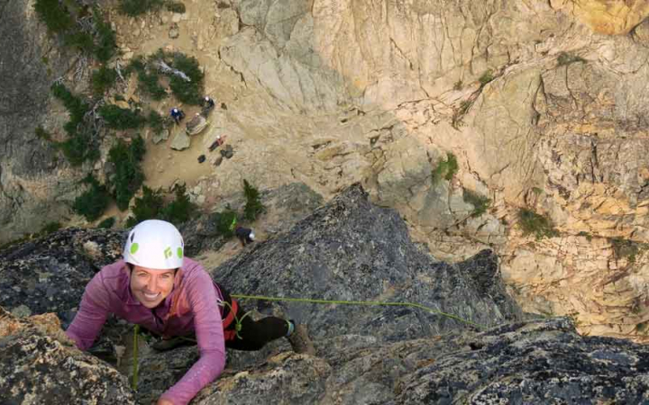a person smiles while looking up as they climb up a rock wall
